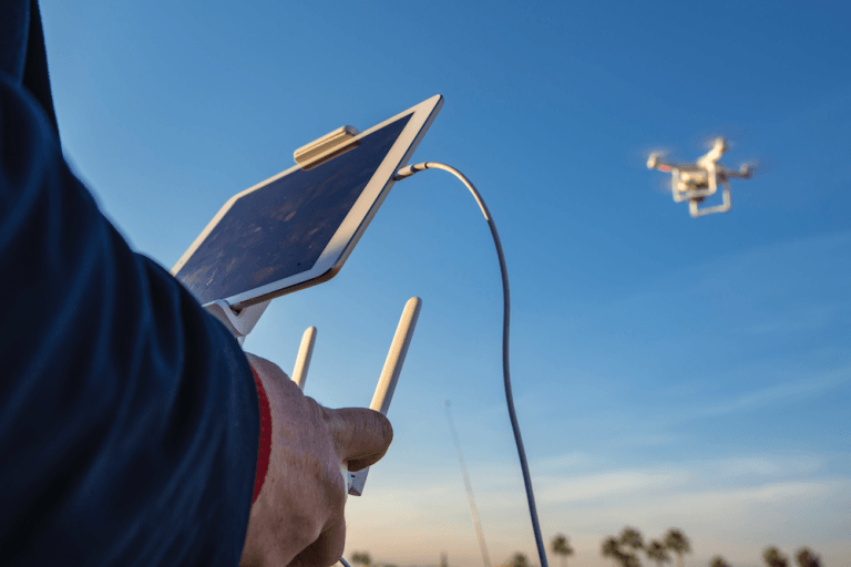 Piloto con un mando y una tableta y un dron volando al fondo